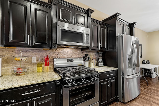 kitchen with light hardwood / wood-style floors, stainless steel appliances, light stone countertops, and decorative backsplash