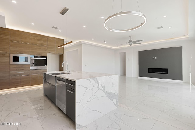 kitchen with appliances with stainless steel finishes, an island with sink, hanging light fixtures, ceiling fan, and a raised ceiling