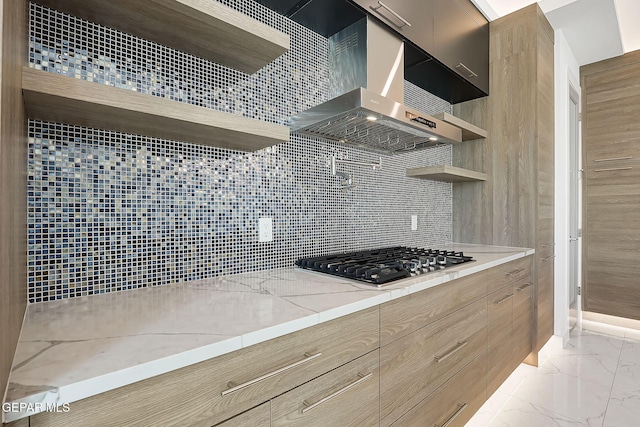 kitchen featuring wall chimney exhaust hood, tasteful backsplash, stainless steel gas stovetop, and light stone counters