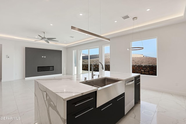 kitchen with sink, hanging light fixtures, a tray ceiling, a center island with sink, and stainless steel dishwasher