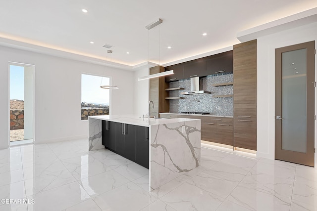 kitchen featuring a breakfast bar, decorative light fixtures, stainless steel gas stovetop, a center island with sink, and wall chimney exhaust hood