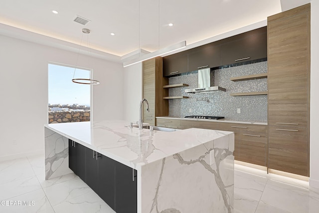 kitchen featuring pendant lighting, sink, stainless steel gas cooktop, a center island with sink, and wall chimney exhaust hood