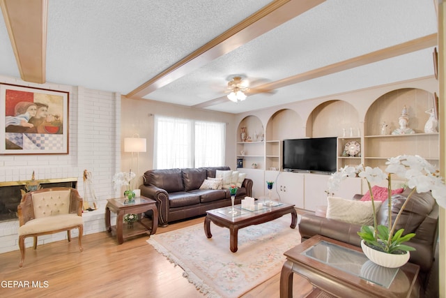 living room with built in features, a fireplace, ceiling fan, light hardwood / wood-style floors, and a textured ceiling