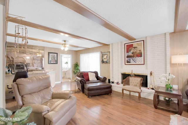 living room featuring beam ceiling, light hardwood / wood-style flooring, a textured ceiling, ceiling fan, and a fireplace