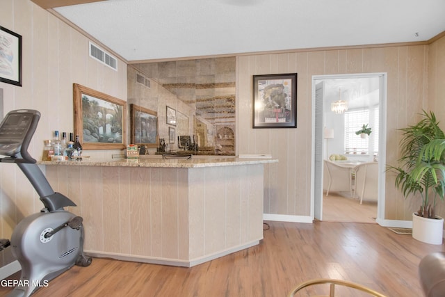 kitchen featuring crown molding, light stone countertops, kitchen peninsula, and light wood-type flooring