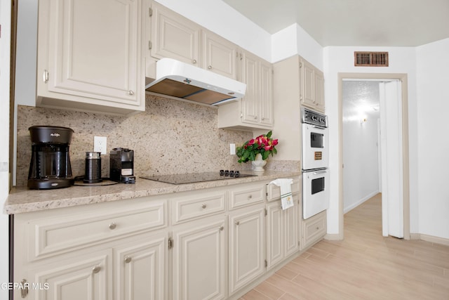 kitchen featuring black electric cooktop, decorative backsplash, white double oven, and light wood-type flooring