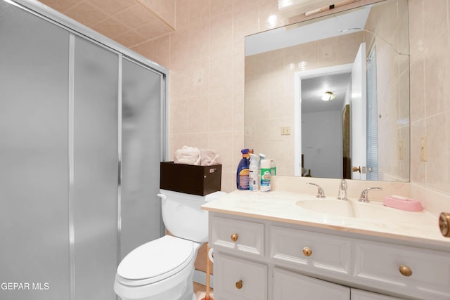 bathroom featuring a shower with door, vanity, tile walls, and toilet