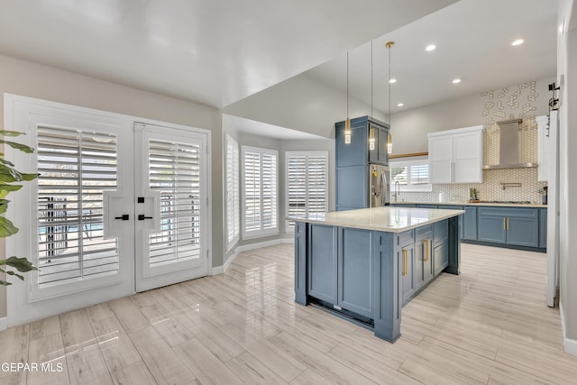 kitchen featuring wall chimney range hood, decorative backsplash, blue cabinets, decorative light fixtures, and french doors