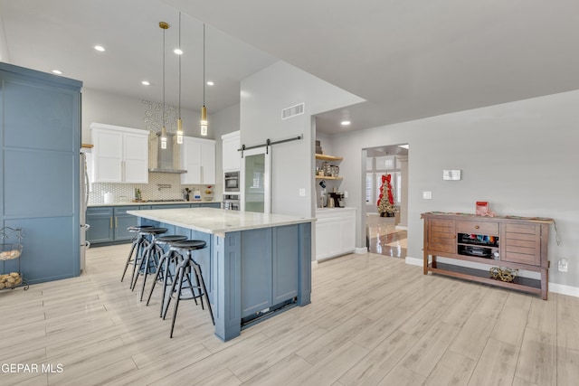 kitchen featuring pendant lighting, a spacious island, white cabinets, decorative backsplash, and a barn door