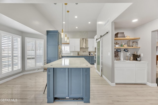 kitchen with pendant lighting, white cabinetry, decorative backsplash, a barn door, and wall chimney exhaust hood