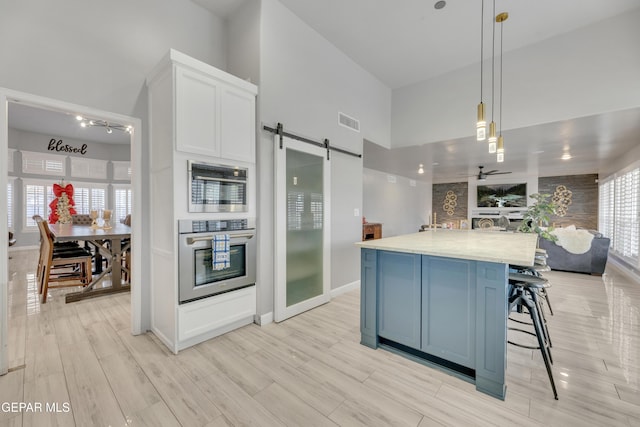 kitchen featuring white cabinetry, stainless steel oven, hanging light fixtures, a barn door, and light hardwood / wood-style floors