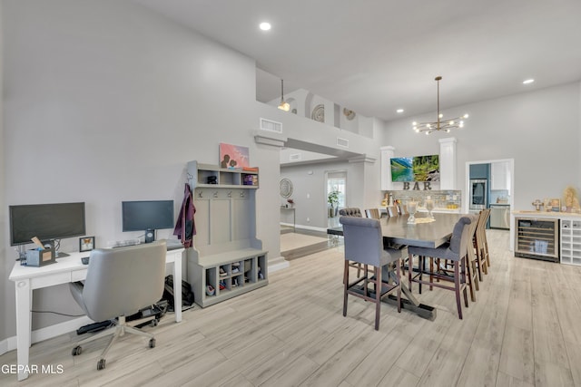 dining space with beverage cooler, a chandelier, and light wood-type flooring