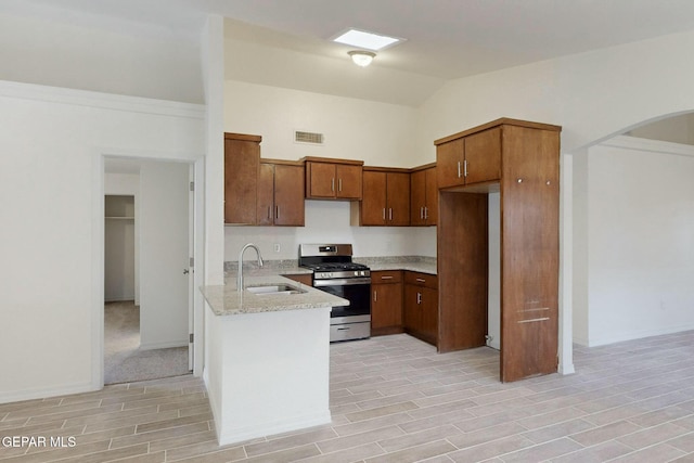 kitchen featuring vaulted ceiling, stainless steel gas range, sink, and light stone countertops