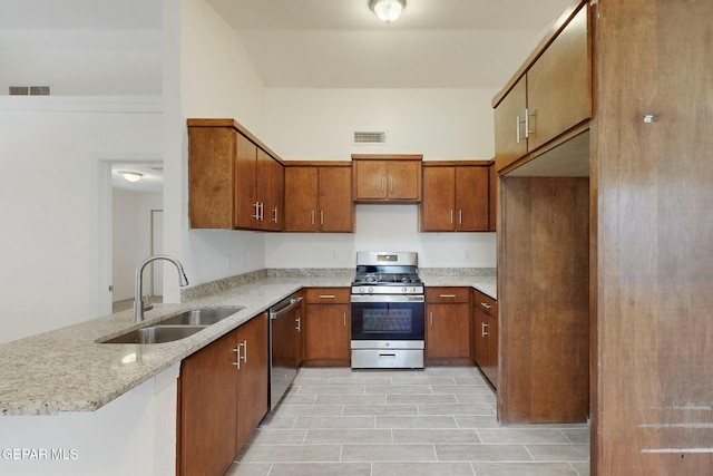 kitchen with light stone counters, stainless steel appliances, kitchen peninsula, and sink