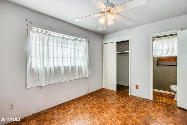 unfurnished bedroom with dark parquet flooring, connected bathroom, ceiling fan, and a closet