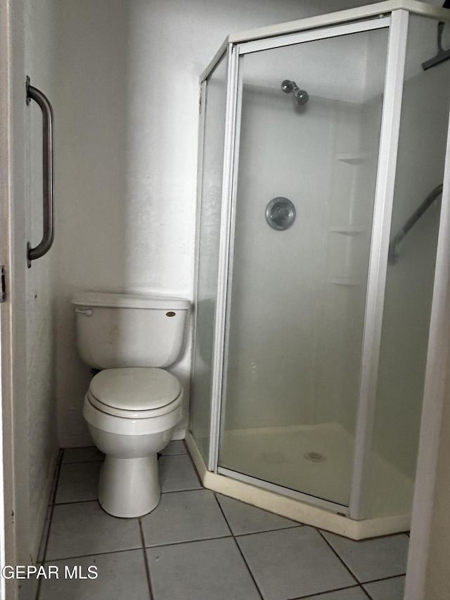 bathroom featuring toilet, a shower with door, and tile patterned flooring