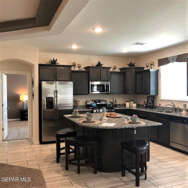 kitchen featuring arched walkways, stainless steel appliances, stone countertops, a kitchen island, and a kitchen bar