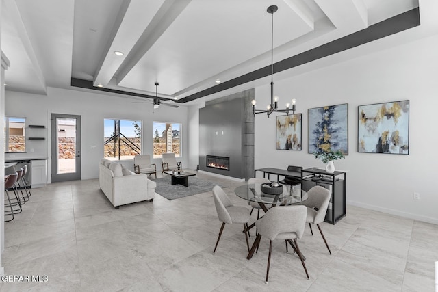 dining room featuring a raised ceiling, a large fireplace, and ceiling fan with notable chandelier