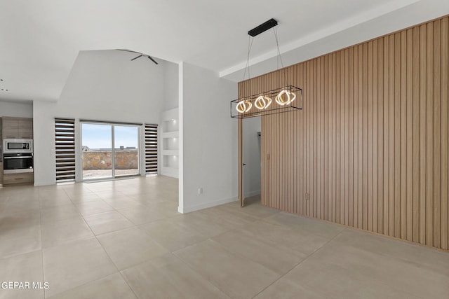 empty room with ceiling fan, a towering ceiling, and wood walls