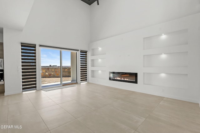 unfurnished living room featuring a high ceiling, light tile patterned flooring, and built in shelves