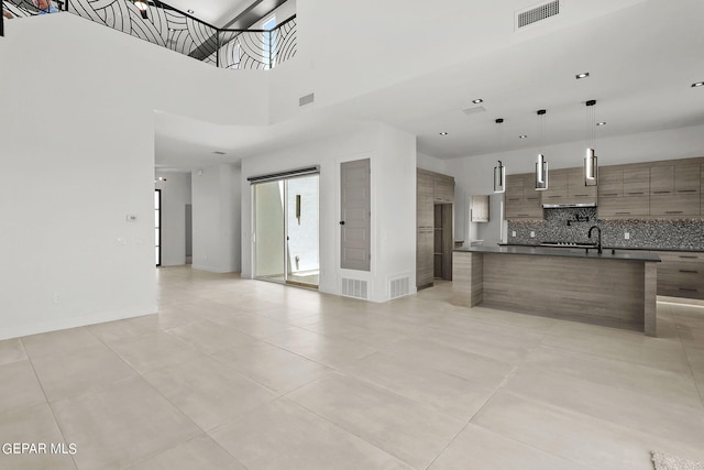 kitchen featuring light tile patterned flooring, sink, backsplash, hanging light fixtures, and a high ceiling