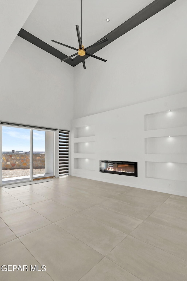 unfurnished living room featuring a towering ceiling, ceiling fan, and built in shelves