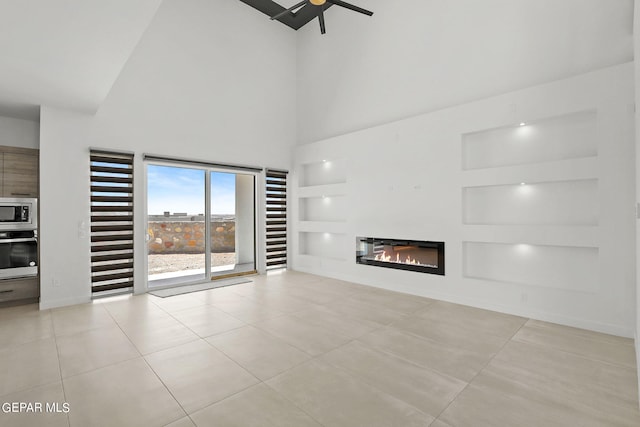 unfurnished living room featuring a high ceiling, light tile patterned flooring, ceiling fan, and built in shelves