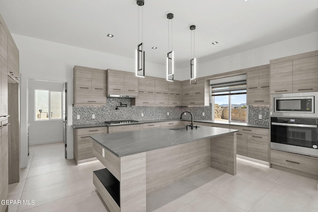 kitchen featuring sink, stainless steel appliances, tasteful backsplash, an island with sink, and decorative light fixtures