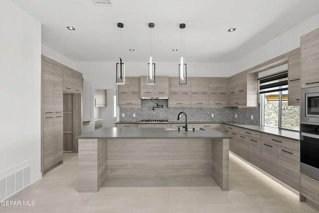 kitchen with sink, stainless steel appliances, tasteful backsplash, a center island with sink, and decorative light fixtures