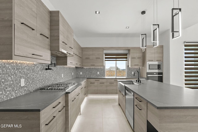 kitchen featuring decorative light fixtures, sink, backsplash, stainless steel appliances, and a center island with sink