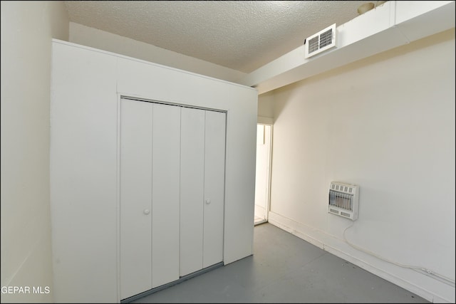 interior space featuring heating unit, concrete floors, a textured ceiling, and a closet