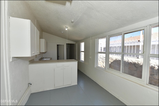 kitchen with vaulted ceiling, plenty of natural light, white cabinets, and a textured ceiling