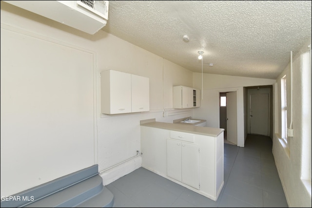 kitchen with lofted ceiling, white cabinets, and a textured ceiling