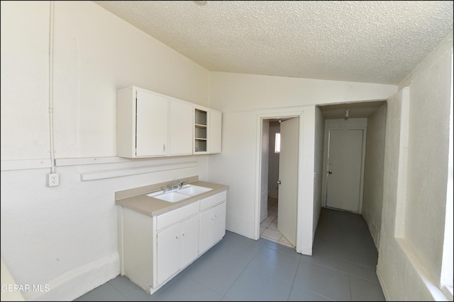 kitchen featuring light tile patterned flooring, sink, vaulted ceiling, a textured ceiling, and white cabinets