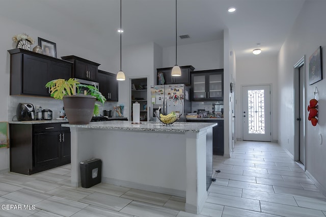 kitchen with decorative light fixtures, tasteful backsplash, an island with sink, stainless steel fridge with ice dispenser, and light stone countertops