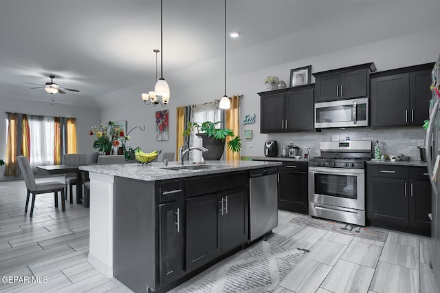 kitchen featuring sink, hanging light fixtures, a center island with sink, appliances with stainless steel finishes, and light stone countertops