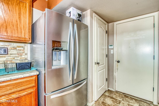 kitchen featuring stainless steel refrigerator with ice dispenser, tasteful backsplash, and a textured ceiling