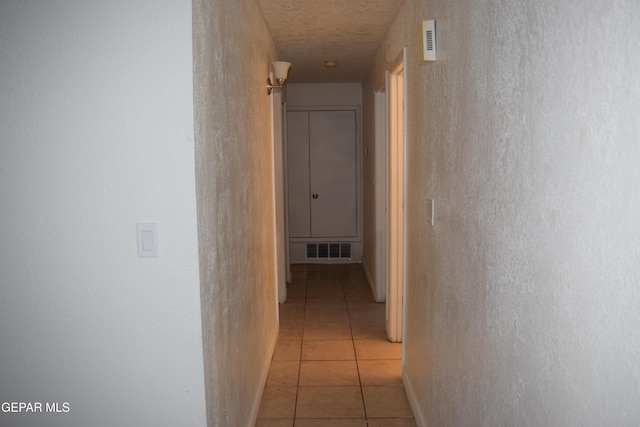 corridor featuring a textured ceiling and light tile patterned flooring