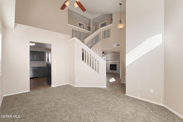 unfurnished living room with ceiling fan, a fireplace, high vaulted ceiling, and dark colored carpet