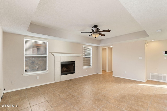 unfurnished living room featuring a raised ceiling, ceiling fan, a textured ceiling, and a fireplace