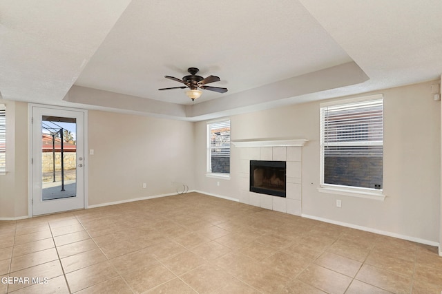 unfurnished living room featuring light tile patterned flooring, ceiling fan, a tray ceiling, and a tile fireplace