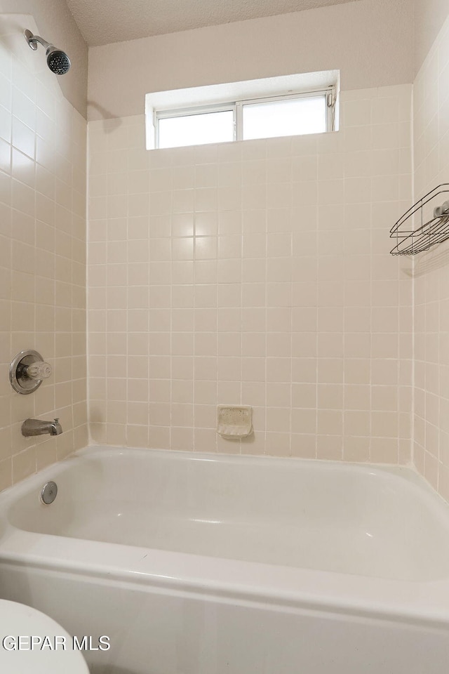 bathroom with toilet, tiled shower / bath combo, and a textured ceiling