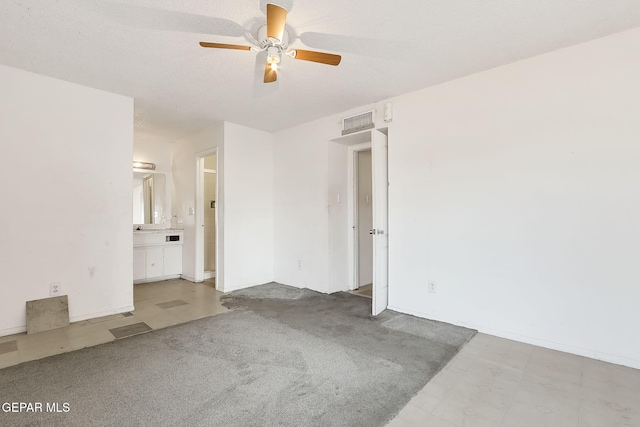 unfurnished bedroom with ceiling fan, light colored carpet, a textured ceiling, and ensuite bathroom