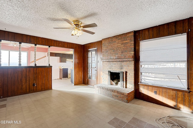 unfurnished living room featuring a brick fireplace, a textured ceiling, ceiling fan, and wood walls