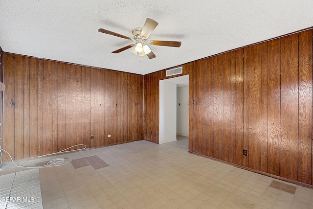 empty room featuring ceiling fan, wooden walls, and a textured ceiling