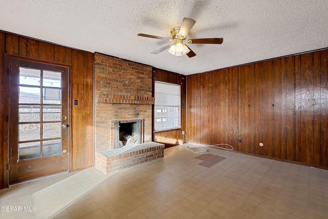 unfurnished living room featuring a fireplace, a healthy amount of sunlight, and wooden walls