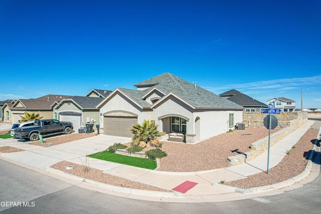 view of front facade featuring stucco siding, a shingled roof, central AC, a residential view, and driveway