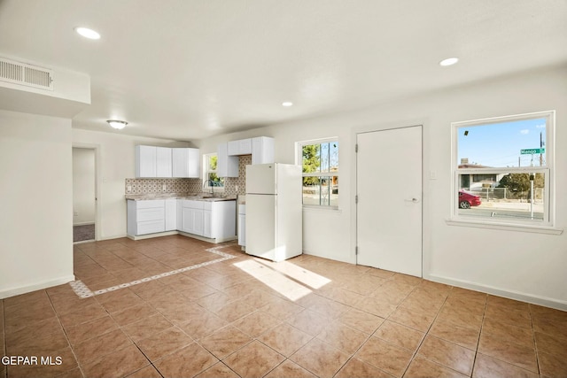 kitchen featuring white fridge, light tile patterned floors, white cabinets, and decorative backsplash