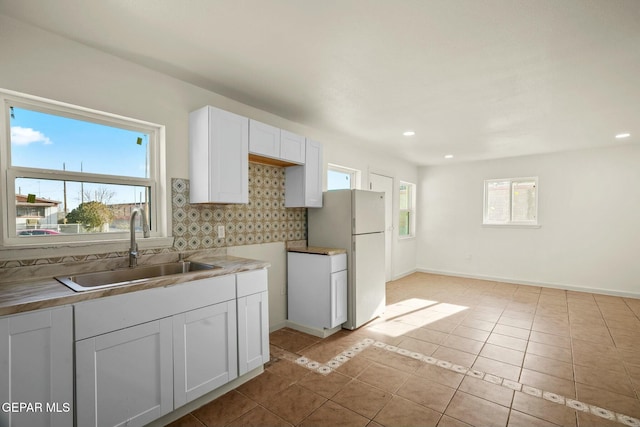 kitchen featuring sink, white cabinetry, backsplash, light tile patterned flooring, and white fridge