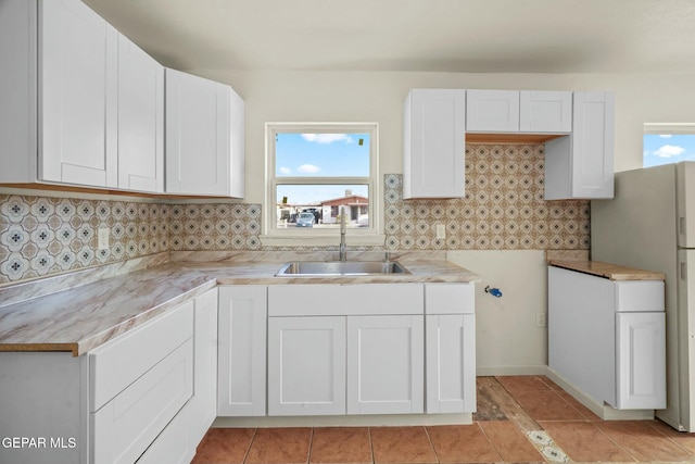 kitchen with refrigerator, sink, decorative backsplash, and white cabinets